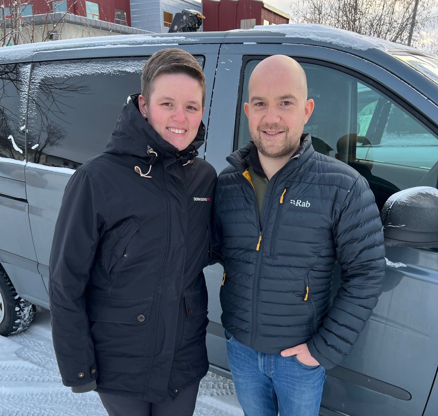 Opplev den kalde skjønnheten i vinterlandskapet sammen med vennene dine. Her ser vi to glade reisende klare for eventyr, med den snødekte bilen som baktepp.
