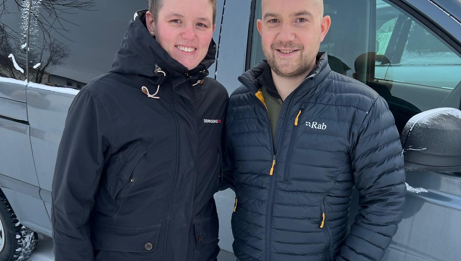 Opplev den kalde skjønnheten i vinterlandskapet sammen med vennene dine. Her ser vi to glade reisende klare for eventyr, med den snødekte bilen som baktepp.