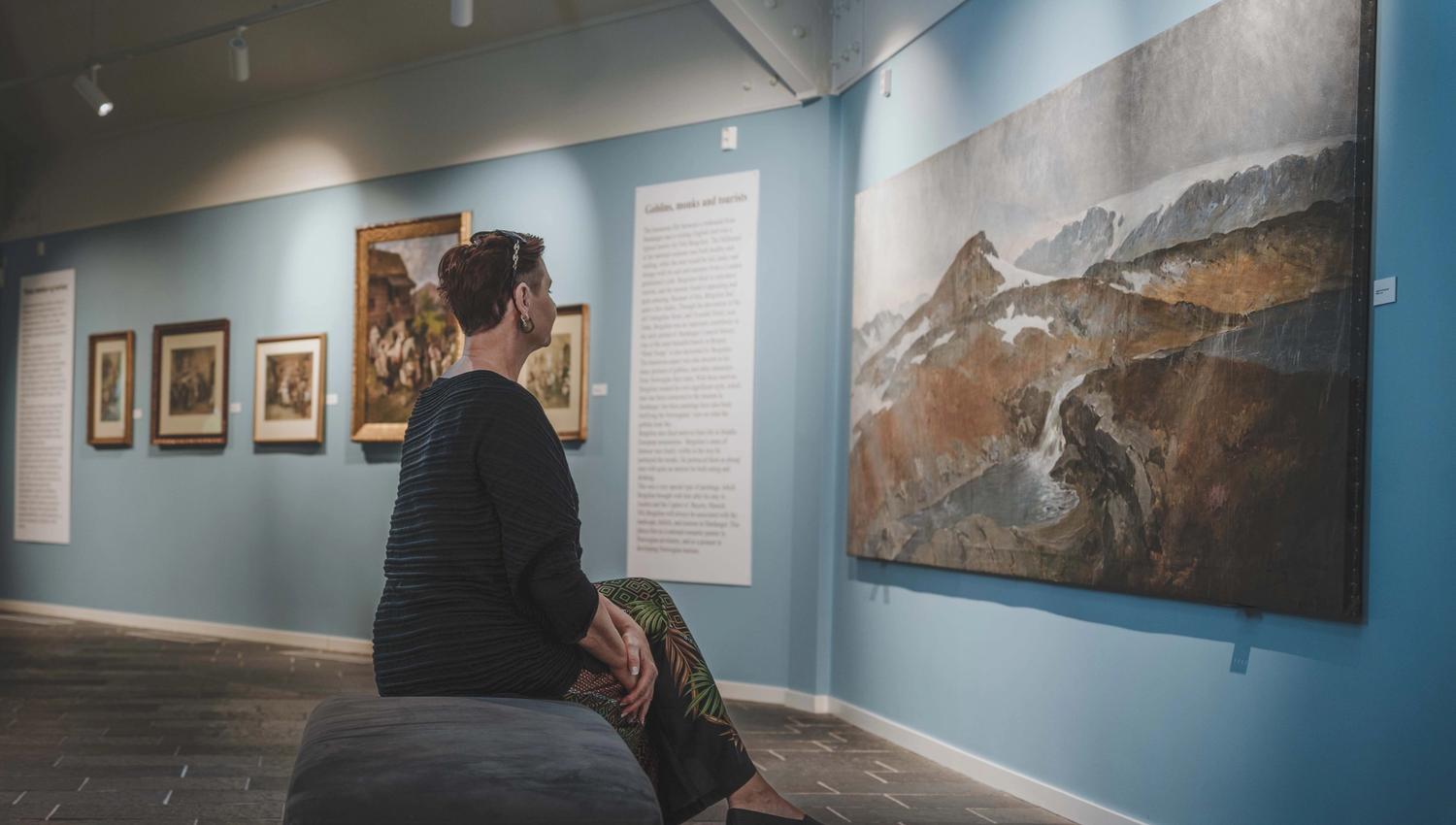 A close up photo of a woman sitting on a bench viewing the paintings.
