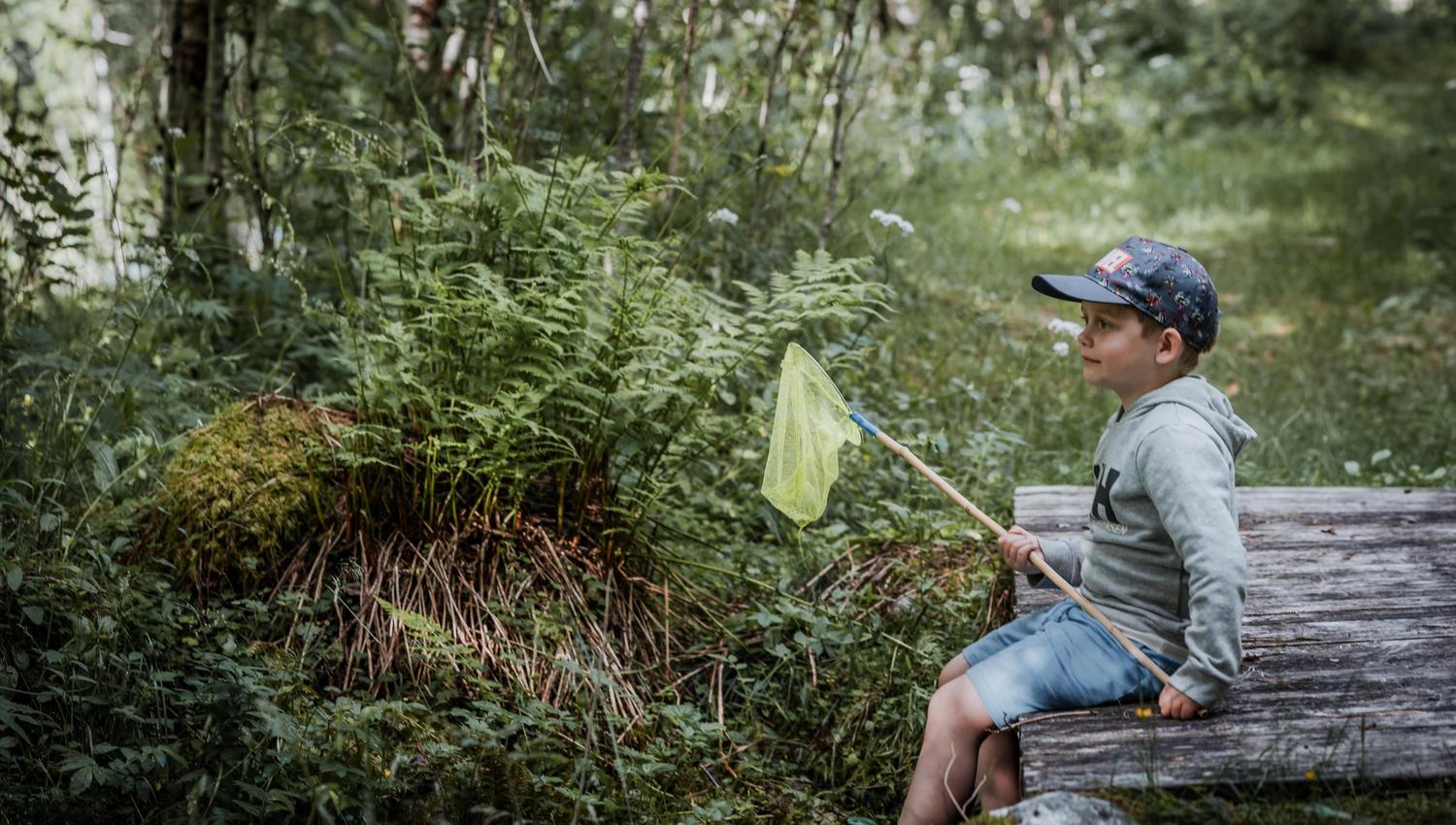 A little boy with a hoof is sitting on a wooden bridge in the woods.