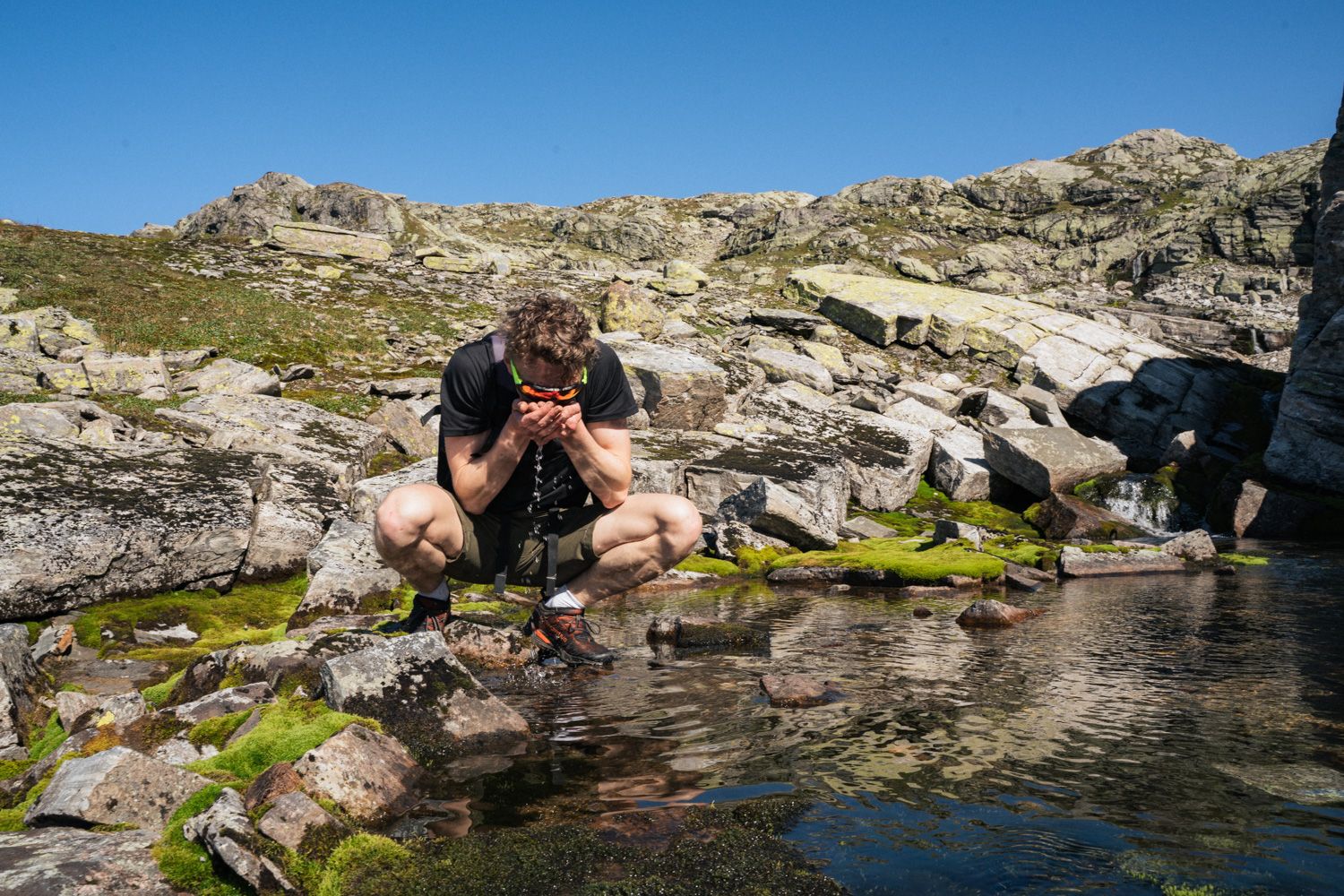 Person drikker vatn frå dam i fjellet.