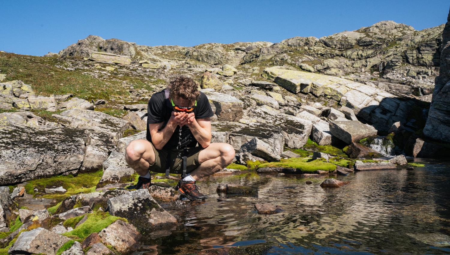 Person drikker vatn frå dam i fjellet.