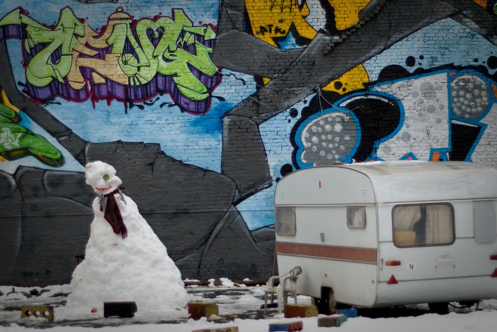 A snowman and a caravan in front of a wall with graffiti.