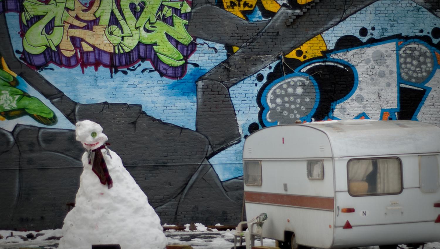 A snowman and a caravan in front of a wall with graffiti.