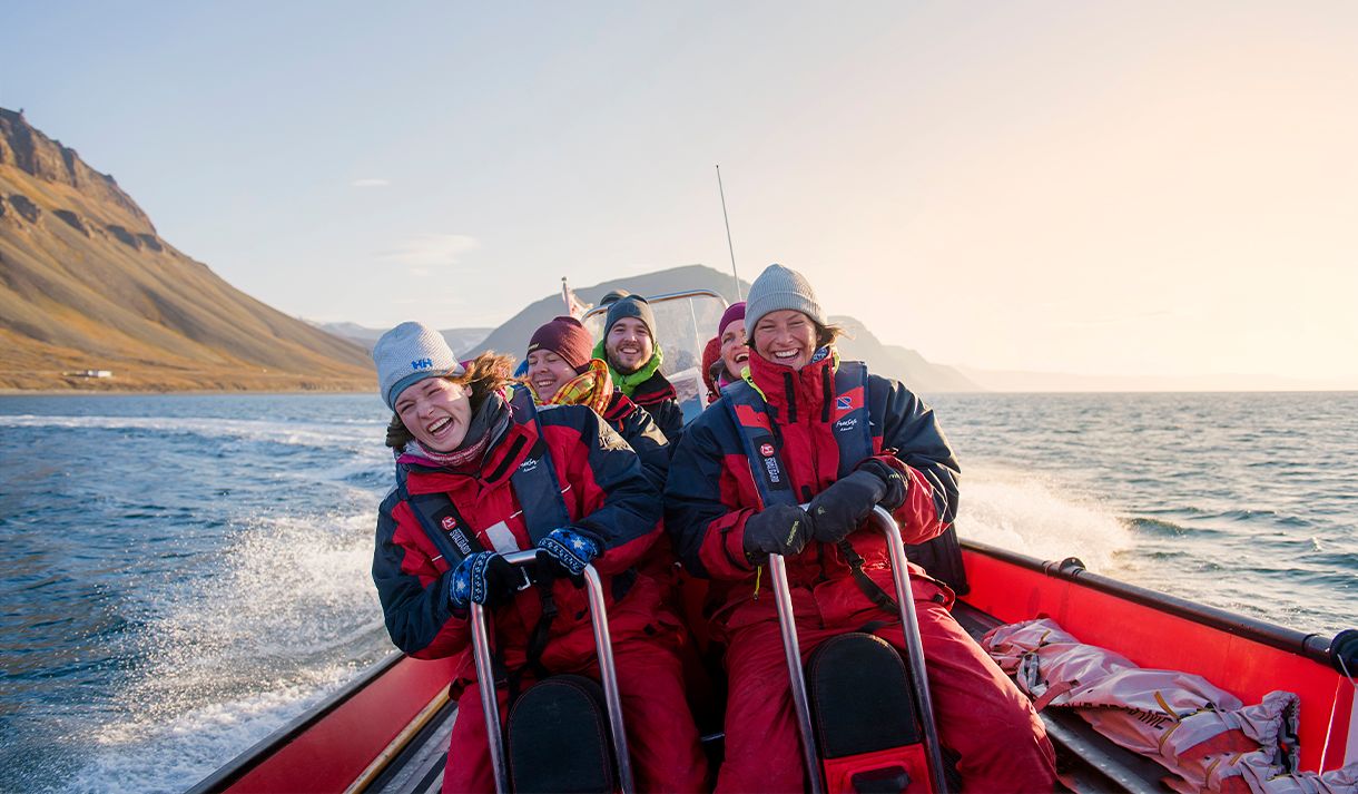 En gruppe med gjester om bord en RIB båt som kjører i fart på en fjord med fjell i bakgrunnen