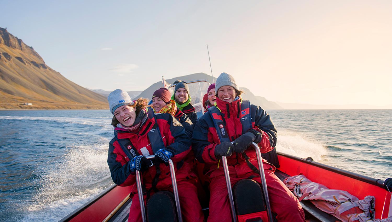 En gruppe med gjester om bord en RIB båt som kjører i fart på en fjord med fjell i bakgrunnen