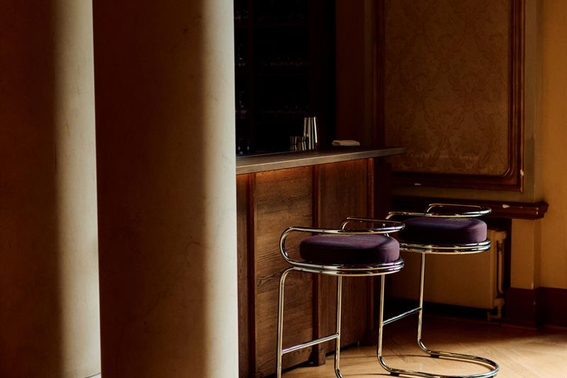 An elegant bar with dark wood, tall stools, and classical columns bathed in warm light.