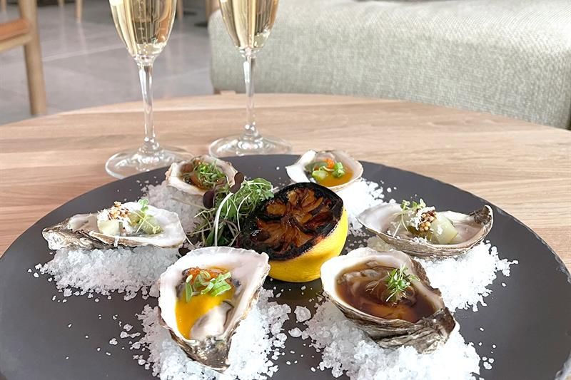 Detail of oyster on a plate with salt sprinkled around and half a lemon in the middle. Two glasses of sparkling white wine next to it.