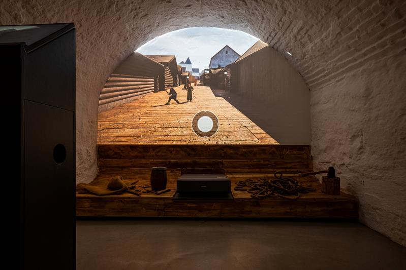 Vaulted room featuring a digital reconstruction of a historic street scene surrounded by wooden structures and maritime objects.