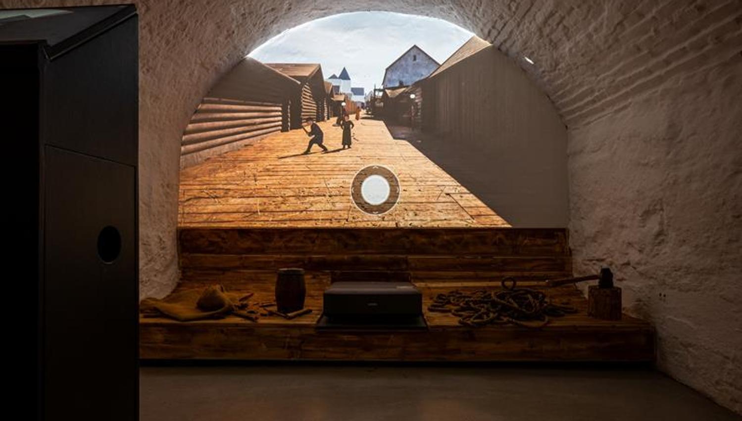 Vaulted room featuring a digital reconstruction of a historic street scene surrounded by wooden structures and maritime objects.