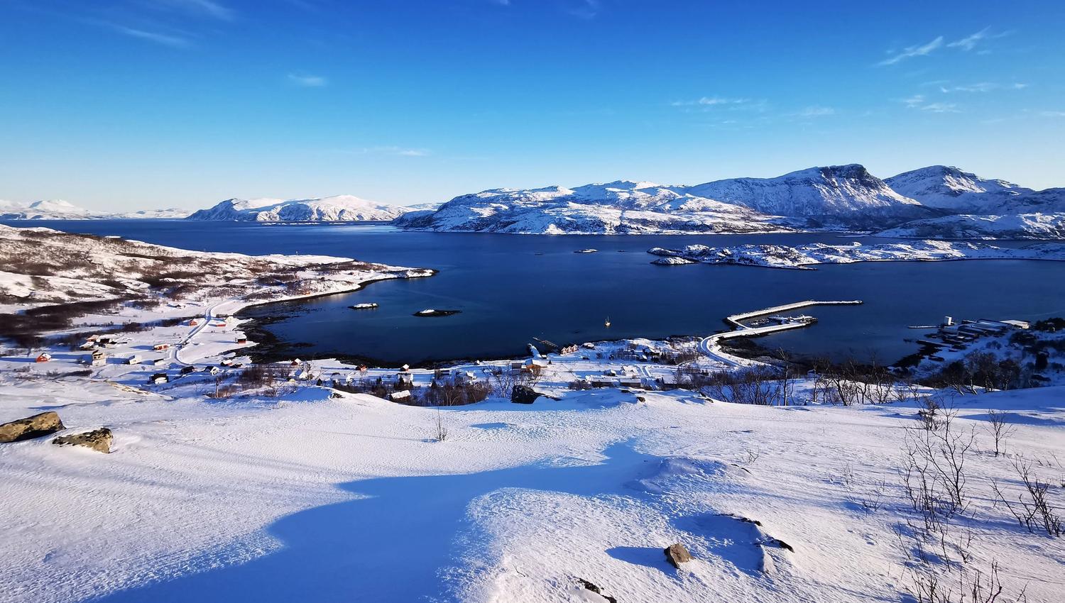 Overview photo of the area of the cabins in winter with the fjord and mountains in front