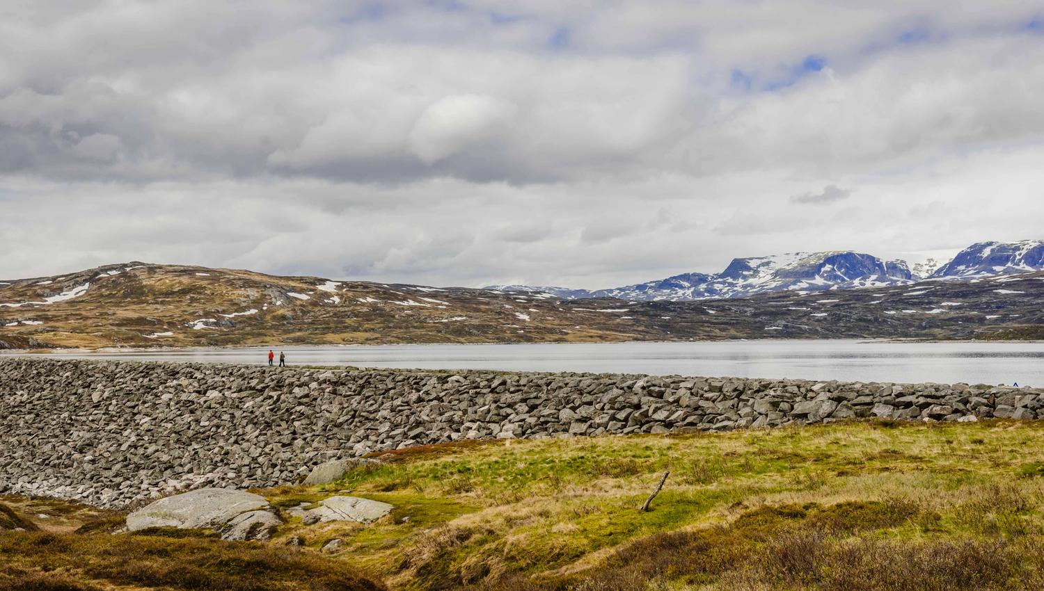 Two persons walking on top of the dam.