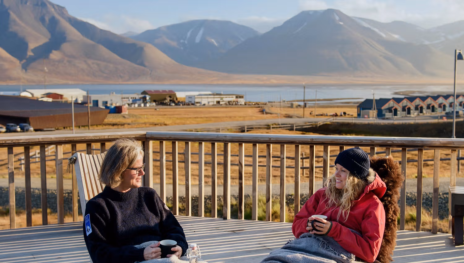 Two guests sitting outdoors with blankets drinking coffee on a balcony