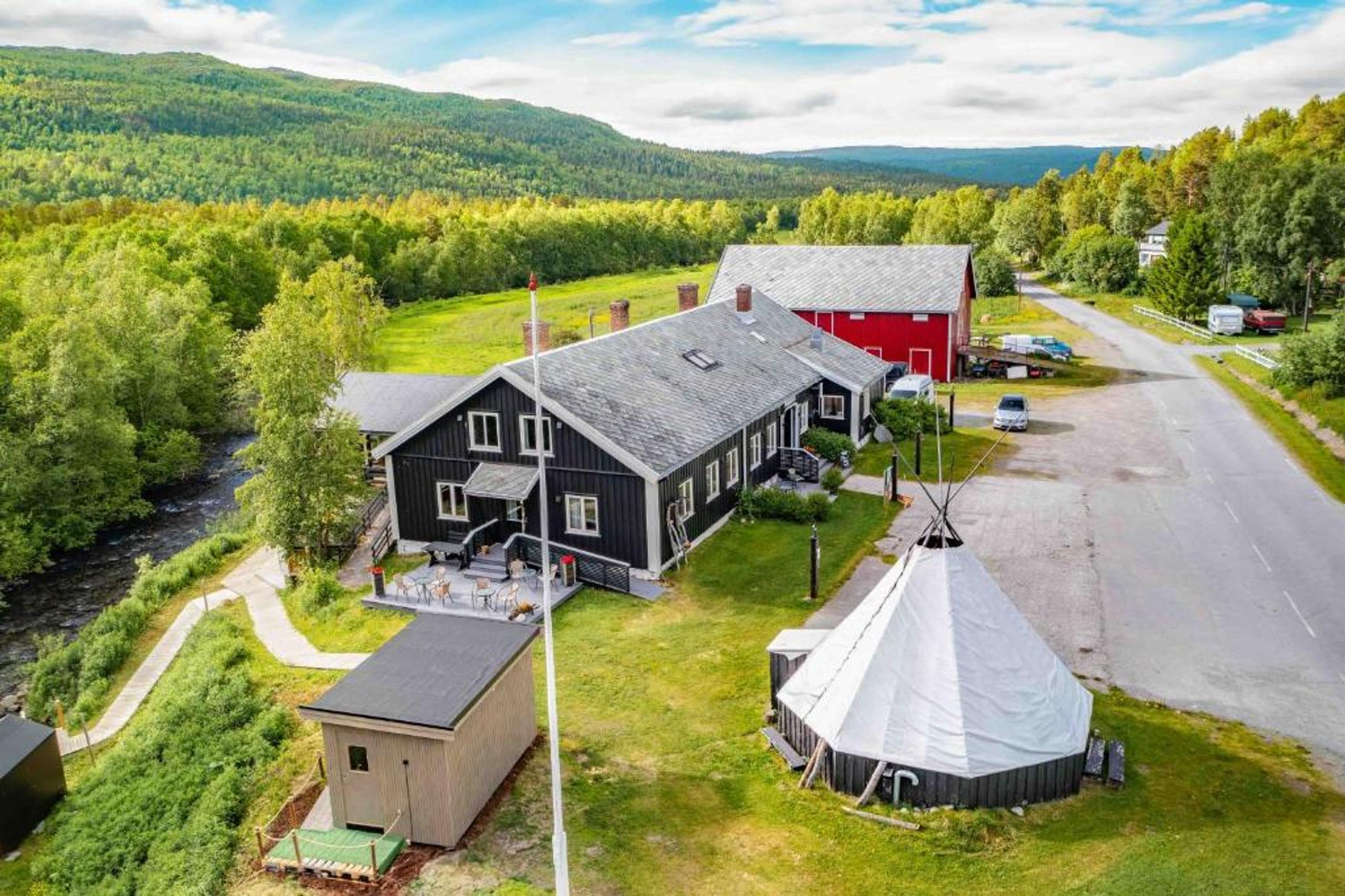 A charming lodge surrounded by lush greenery and mountains with a river nearby.