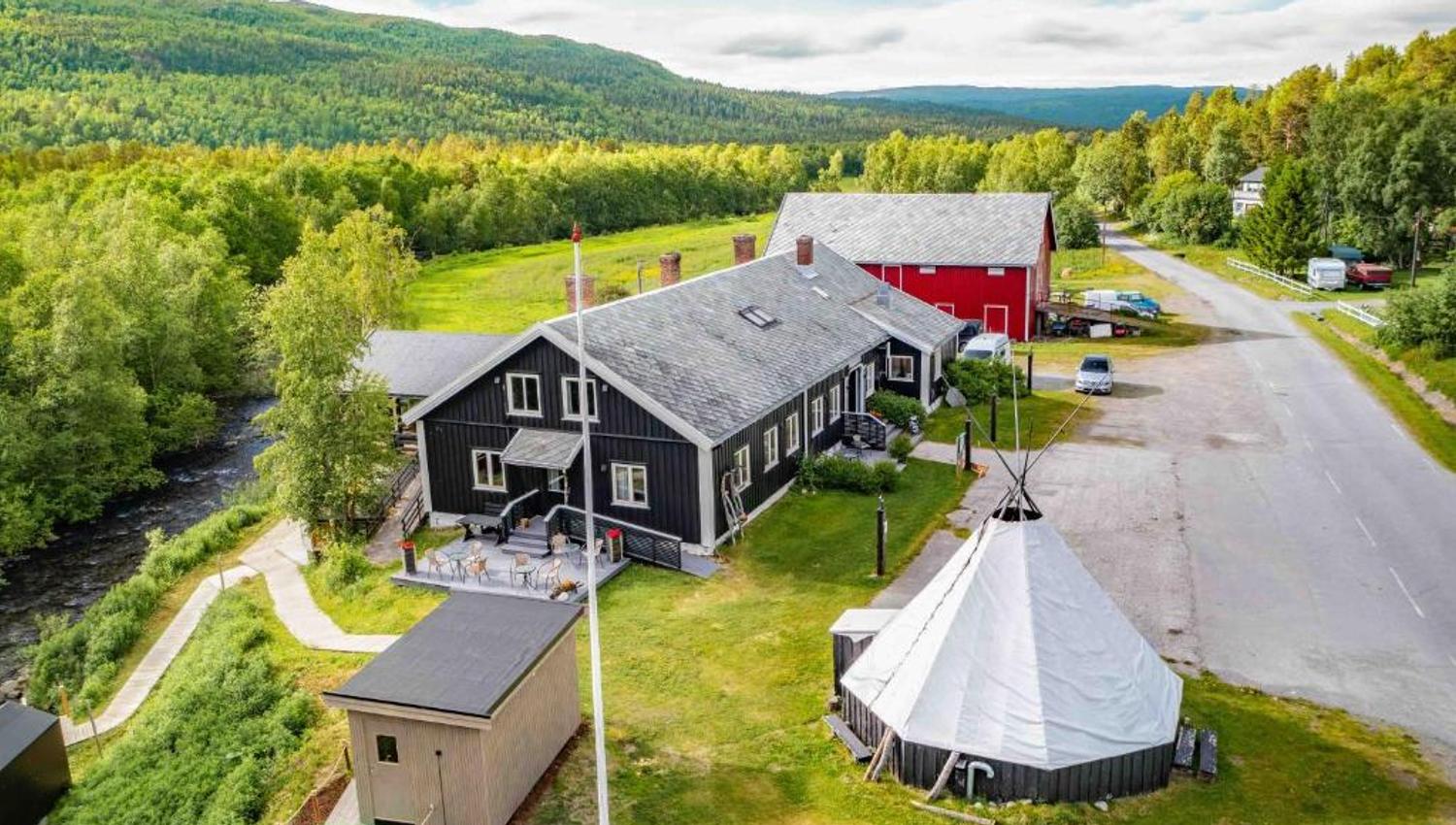 A charming lodge surrounded by lush greenery and mountains with a river nearby.