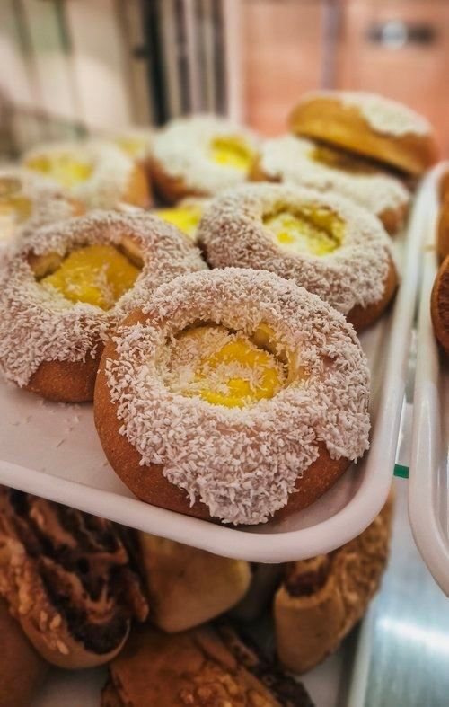 Close-up of round pastries coated in shredded coconut with yellow custard centers on a white tray in a bakery case.