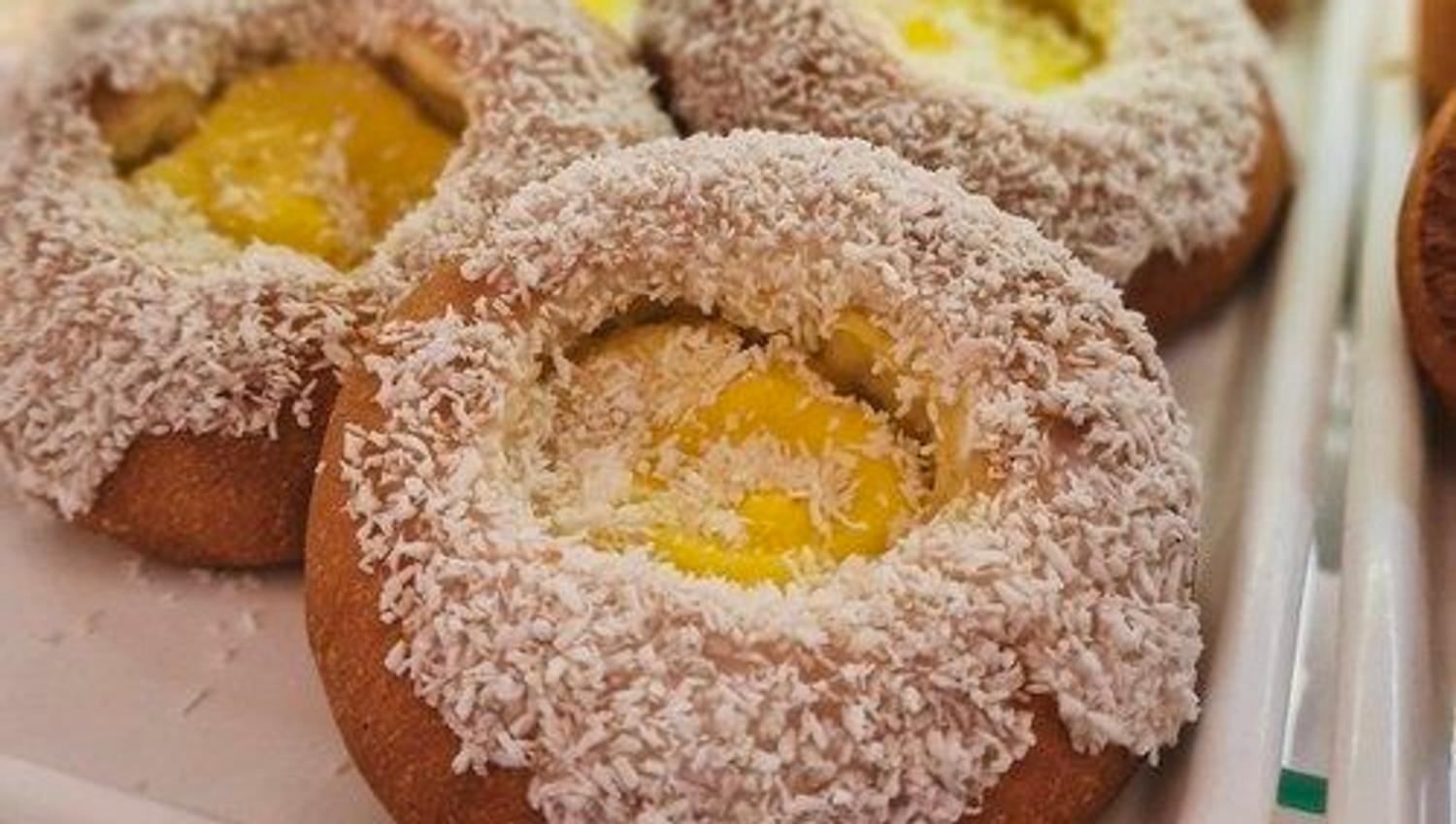 Close-up of round pastries coated in shredded coconut with yellow custard centers on a white tray in a bakery case.