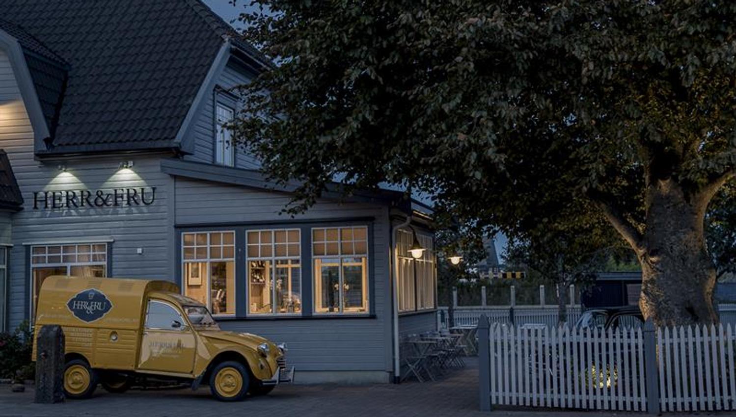 Facade at night: gray restaurant. Yellow delivery van parked at the restaurant.