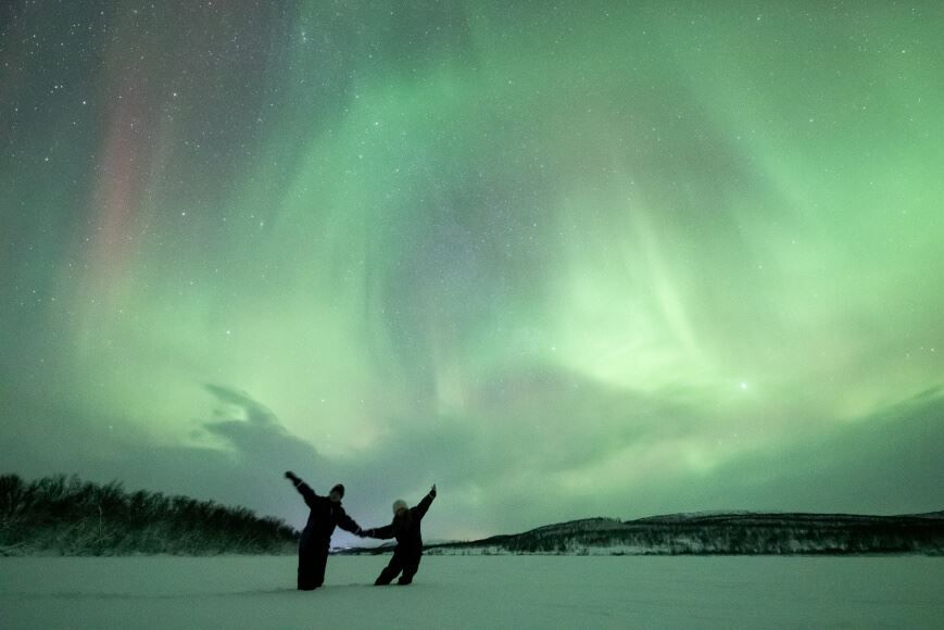 Two guests posing under northern lights
