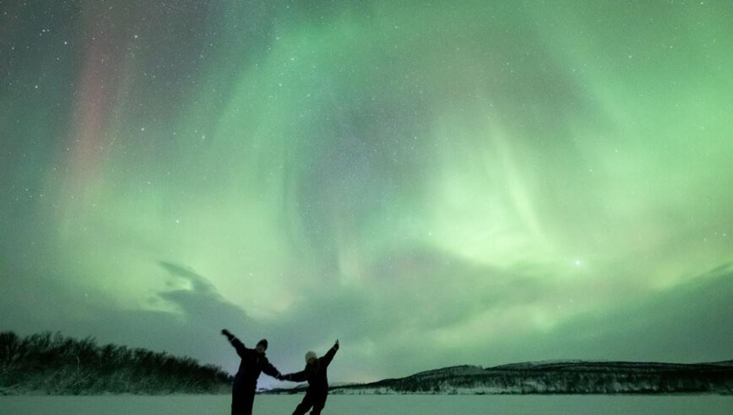 Two guests posing under northern lights