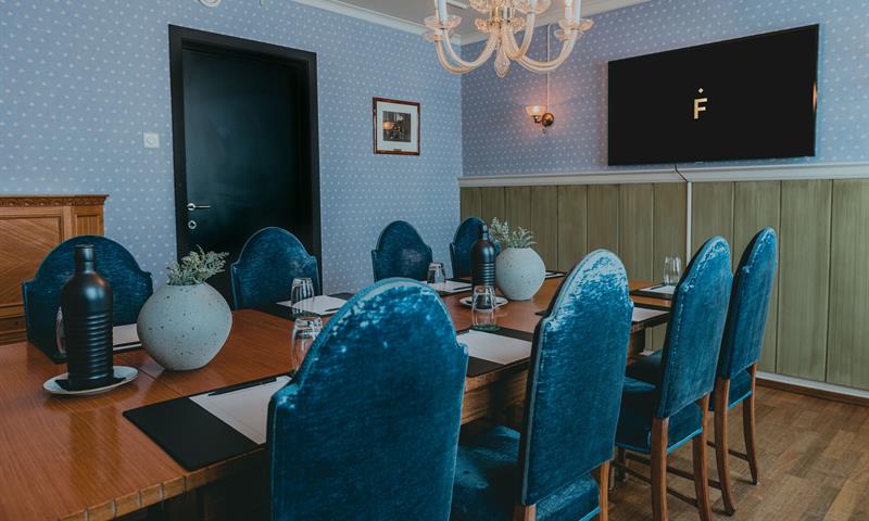 A meeting room with a table, blue chairs and walls, as well as a screen