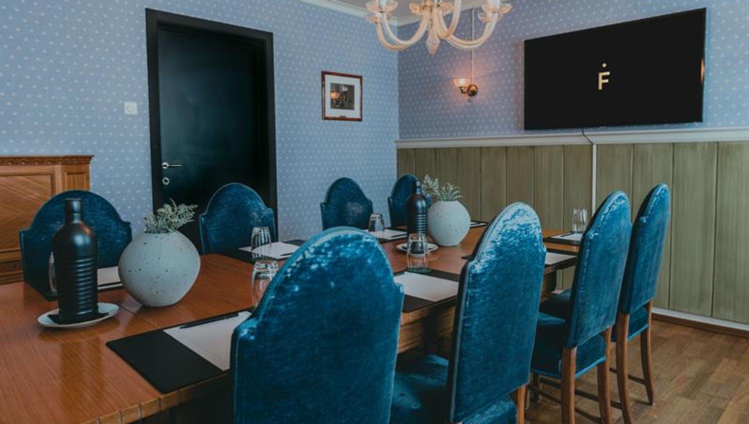 A meeting room with a table, blue chairs and walls, as well as a screen