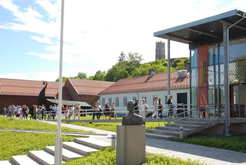 Hvitt trehus, glassbygning og mange mennesker som går inn på museet.