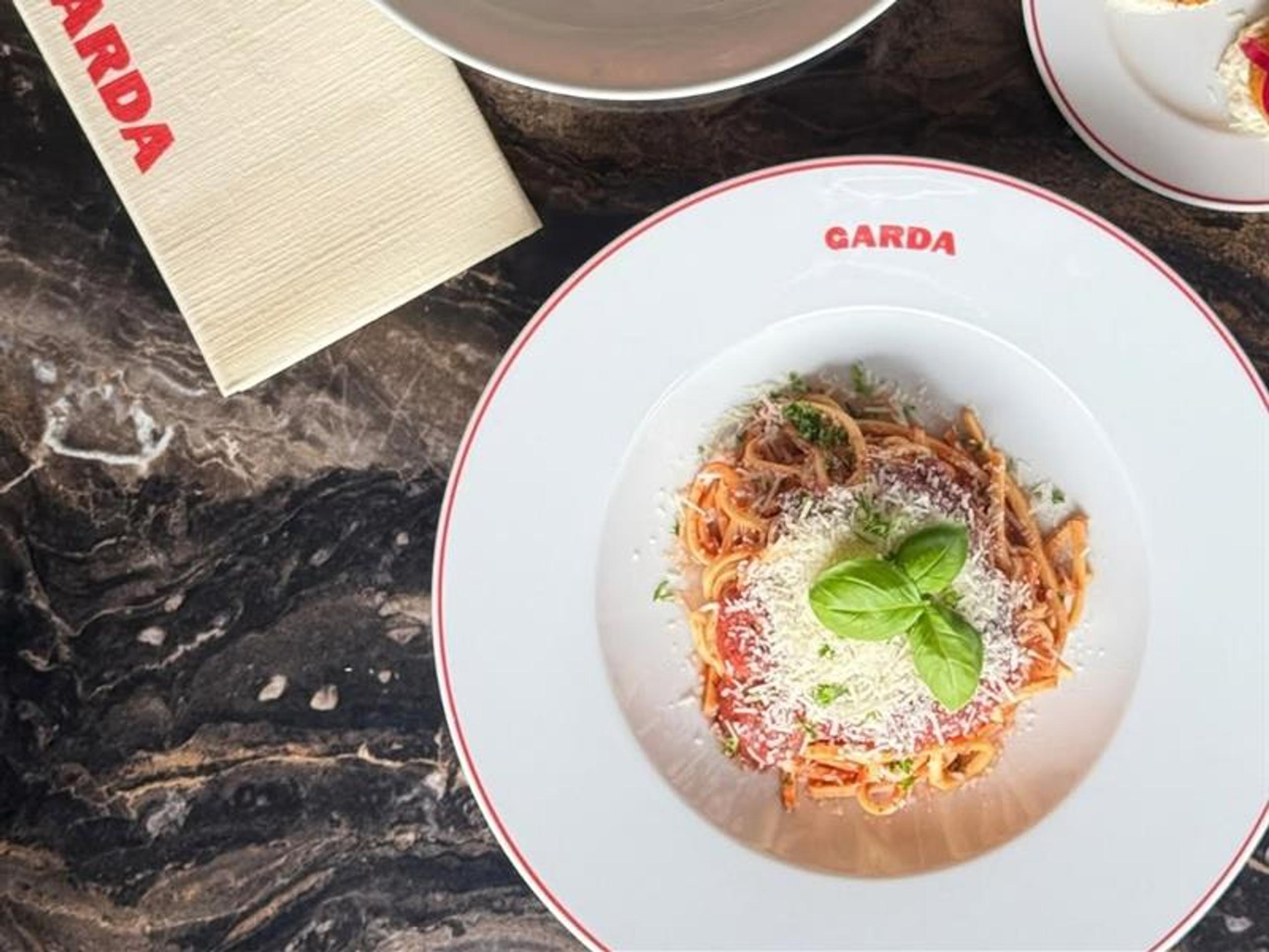 Italian dishes served on plates with the Garda logo, photographed from above on a dark table.