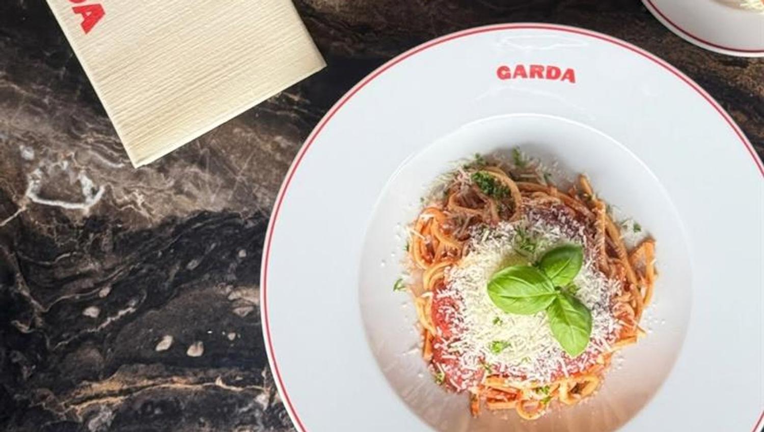 Italian dishes served on plates with the Garda logo, photographed from above on a dark table.