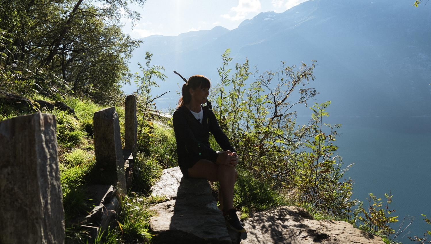 A woman sitting on a bench with the Hardangerfjord in the background.