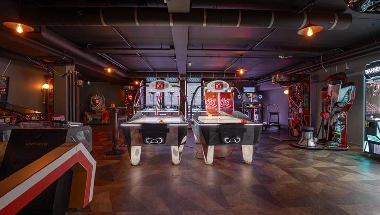 Games area with air hockey tables, arcade machines and boxing machines in a modern venue with atmospheric lighting