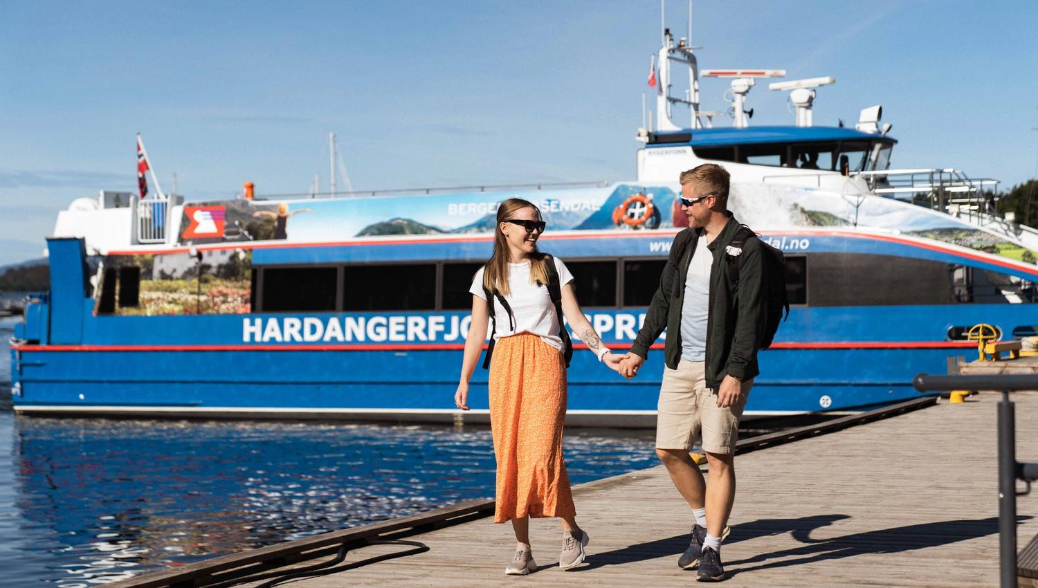 A couple walking on the dock beside Hardangerfjordekspressen, ready for a boat trip in Hardanger.