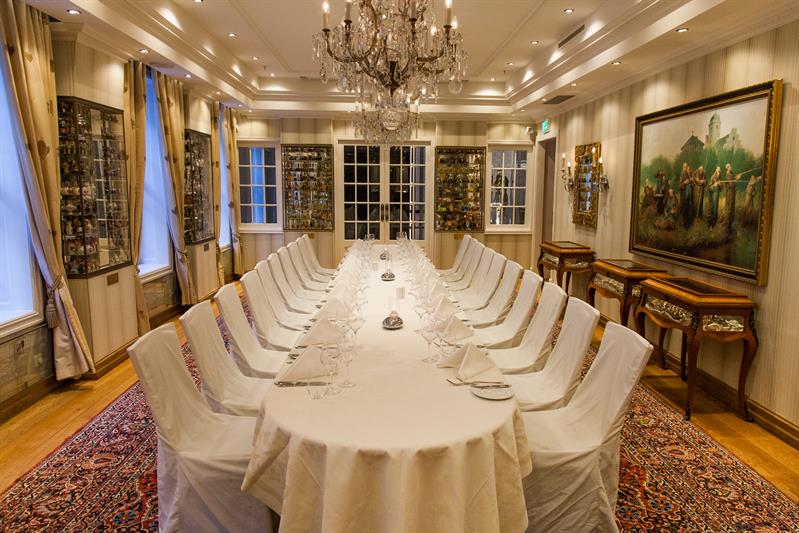 Long table set for dining with white tablecloth, chairs, paintings on the walls, chandelier in the ceiling