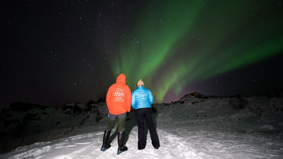 Two guests experience the Northern Lights beneath the Arctic night sky on a guided tour from Tromsø.