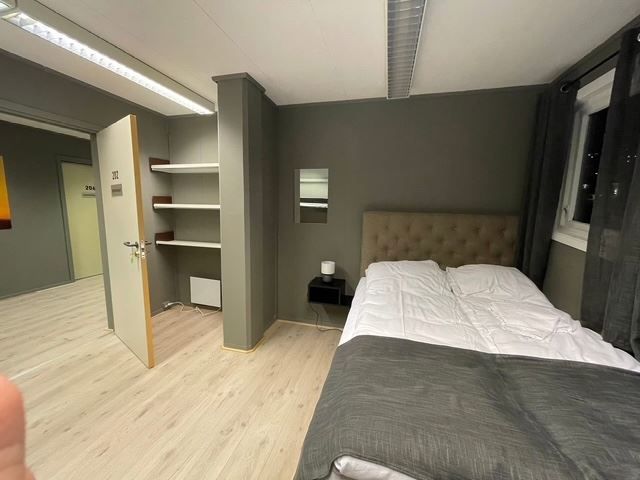 Modern bedroom with a double bed, gray walls, open shelves, bedside table, window curtains, and open door.
