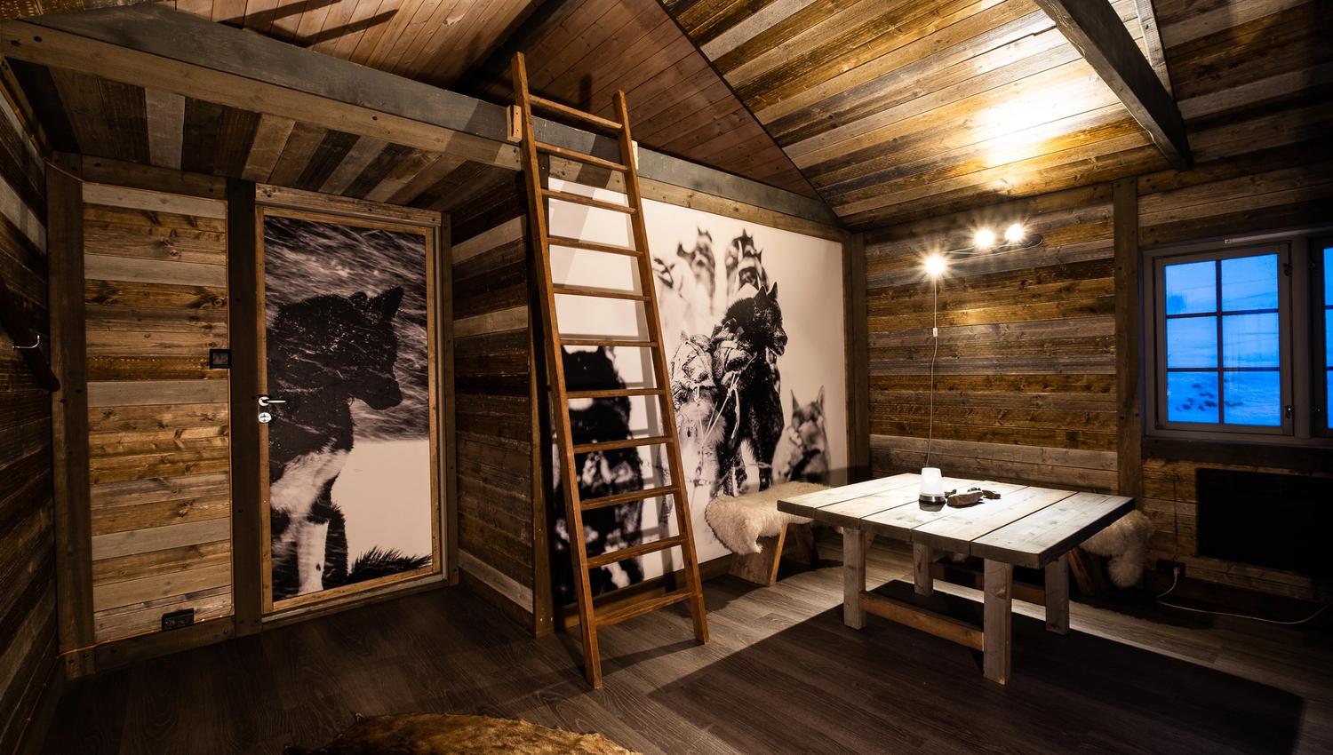Interior photo of Tommy's Lodge, with a dining table, a ladder to a loft and photos hanging on the walls