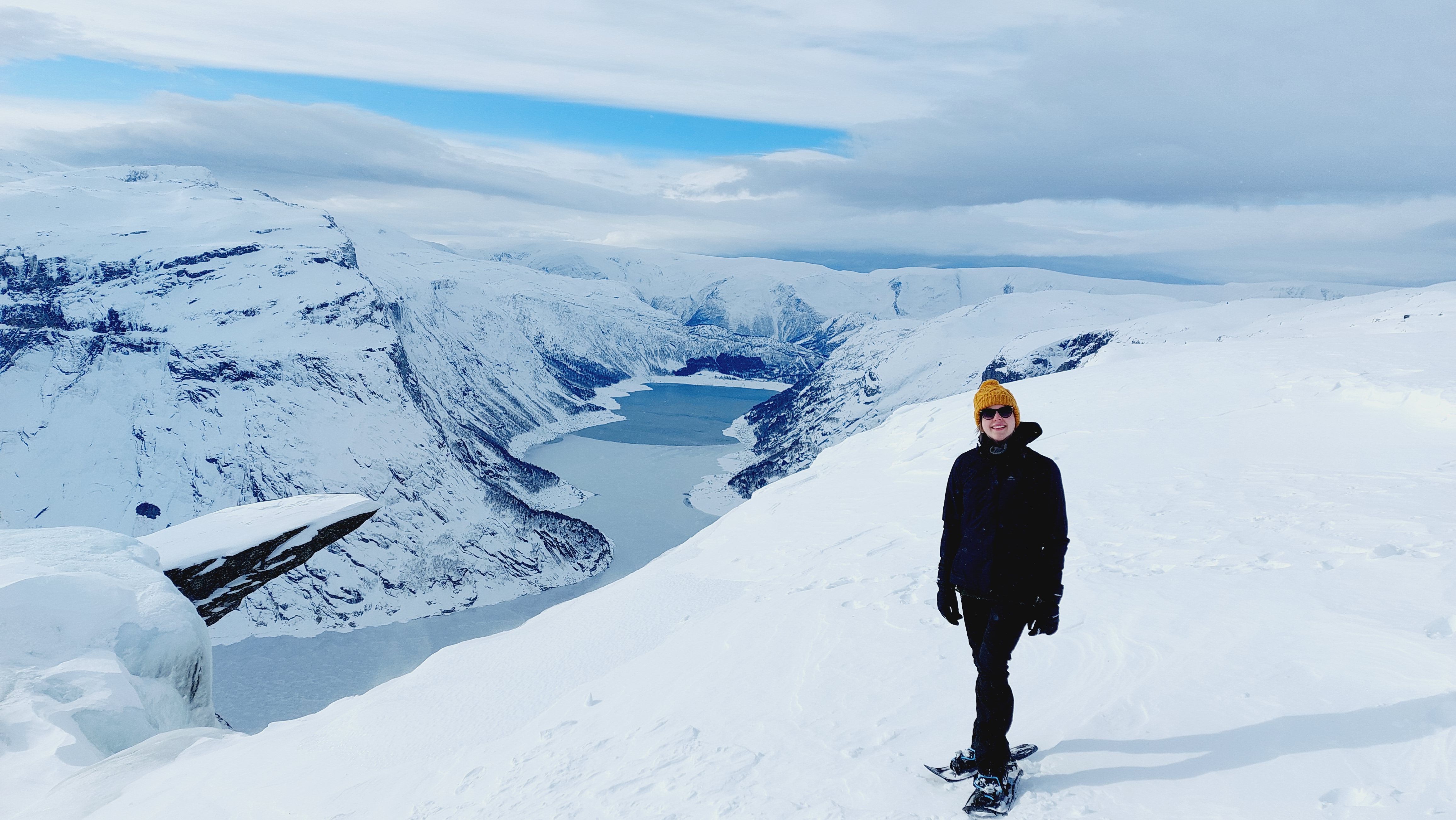 Hiker with a yellow hat standing at the winter viewpoint near Trolltunga.