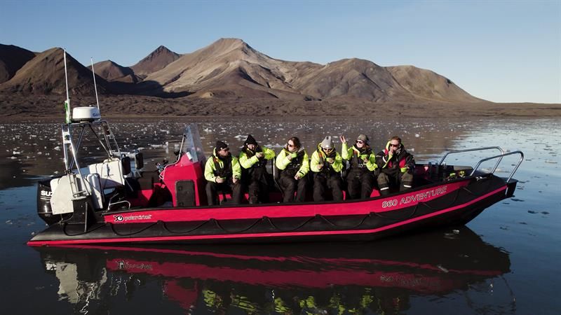 RIB boat with passengers in yellow suits on mirror-calm water with mountains behind.