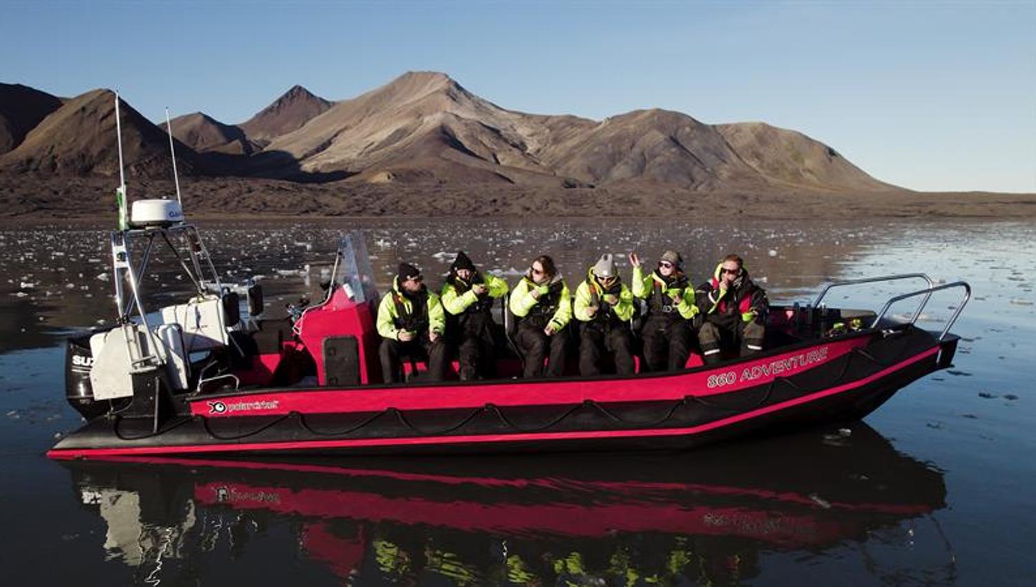 RIB boat with passengers in yellow suits on mirror-calm water with mountains behind.