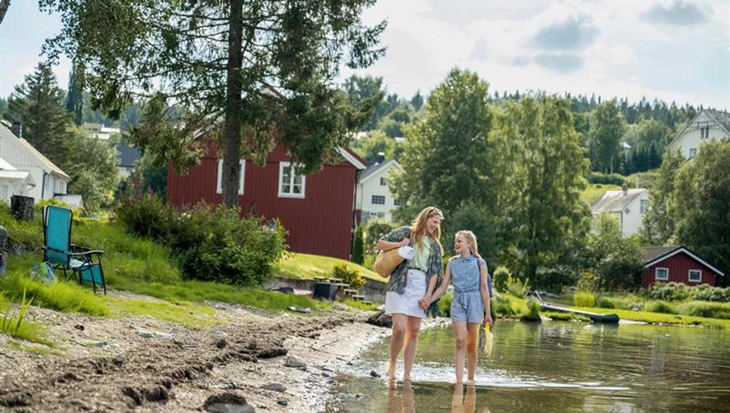 Mamma og jente vasser i vannkanten av Snåsavatnet nedenfor Garveriet i Viosen