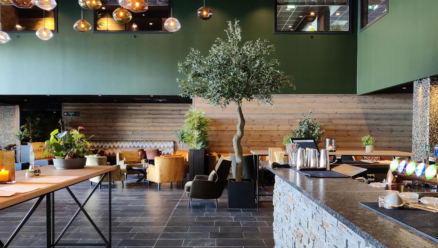 Restaurant interiour with slate floor, stone bar counter, a warm wooden panel on the wall with green shielding and many warm yellow hanging lamps. An