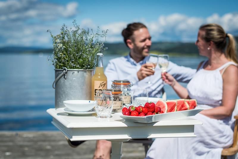 To personer som sitter og skåler ved et bord med jordbær og vannmelon på.
