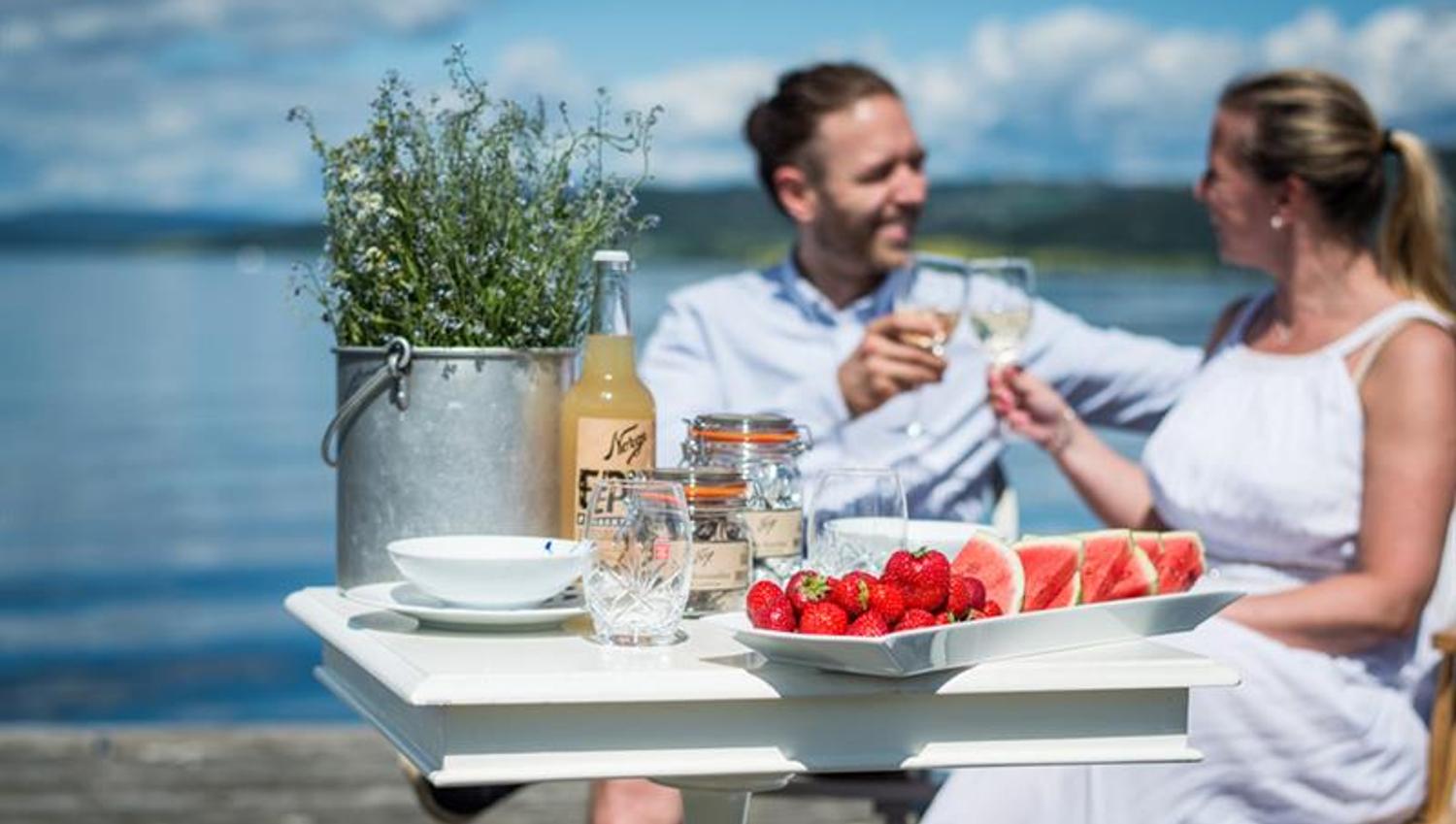 To personer som sitter og skåler ved et bord med jordbær og vannmelon på.