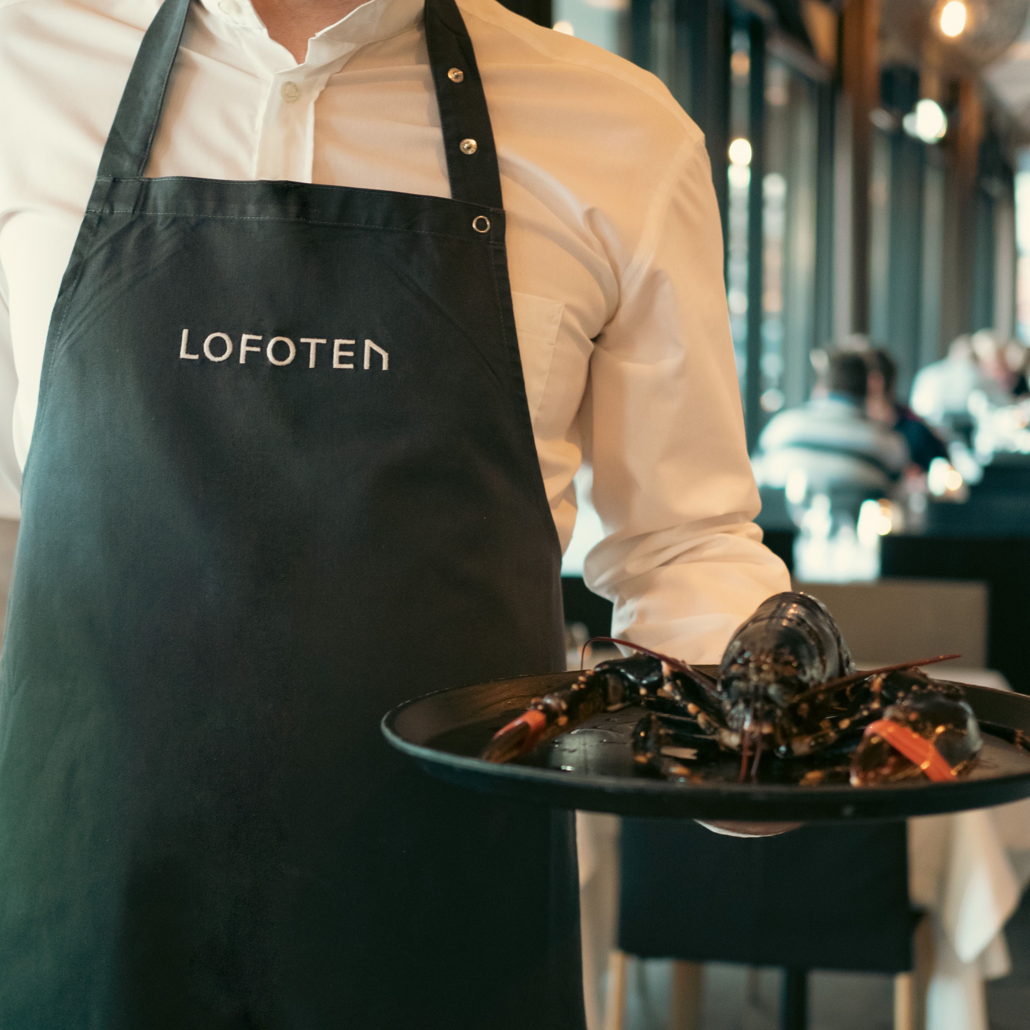 Man in an apron holding a tray with a lobster on it