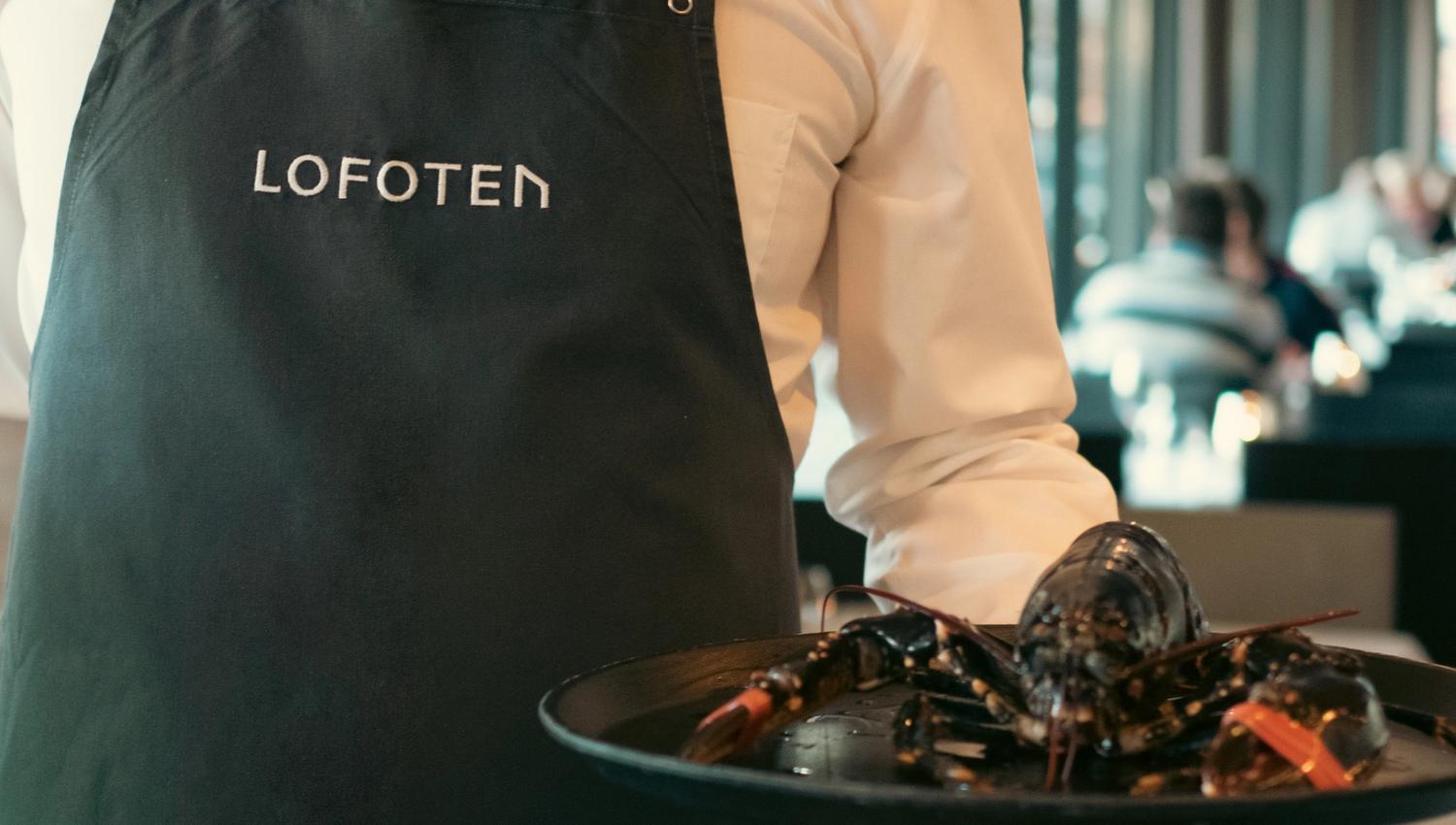 Man in an apron holding a tray with a lobster on it