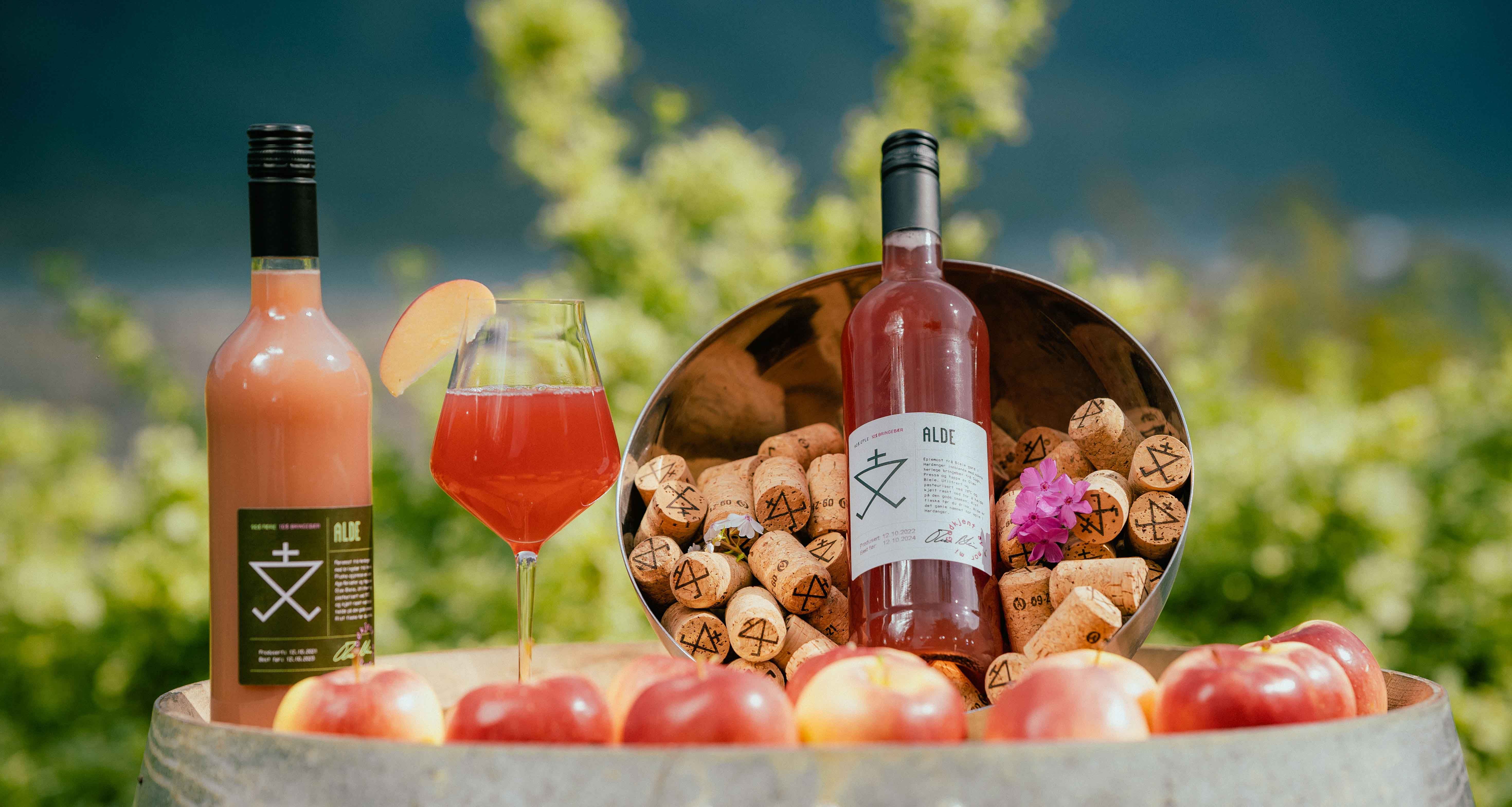 Bottle and glass of Alde cider surrounded by apples and corks in Hardanger.