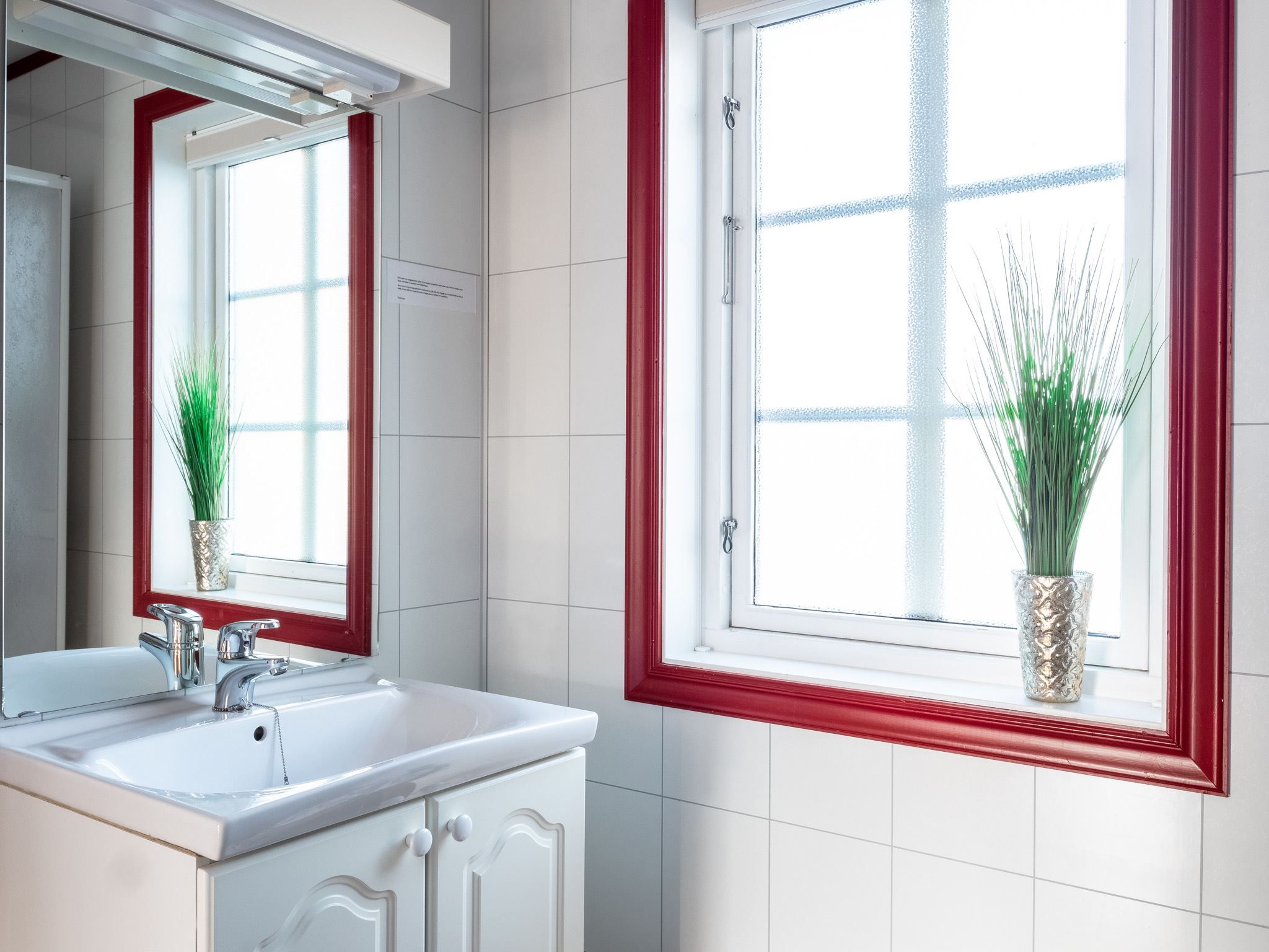 Bathroom with a white sink, mirror and window with red frames, and a plant on the windowsill