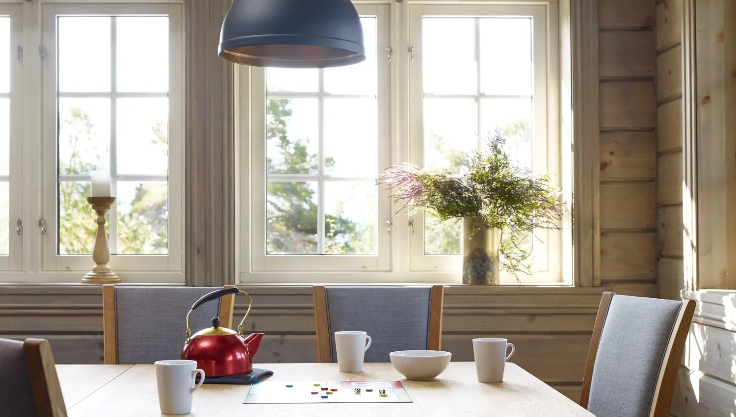 Lyst spisehjørne i trepanel med bord, fire stolar, raud tekjele, koppar og taklampe framfor vindauge ved Furuvins Lodge..