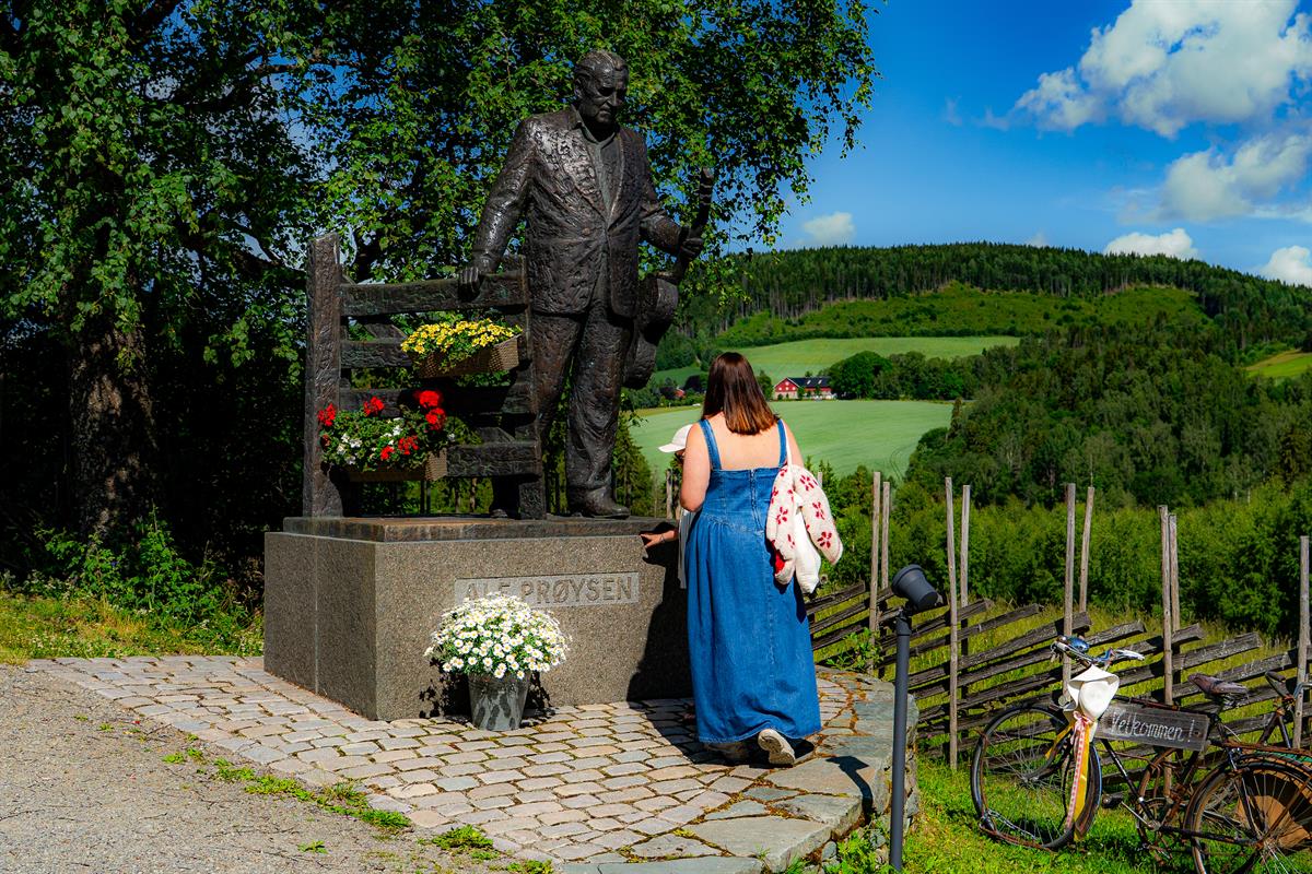 Prøysenhuset i Ringsaker. Mor og sønn foran statue av Alf Prøysen ved inngangen