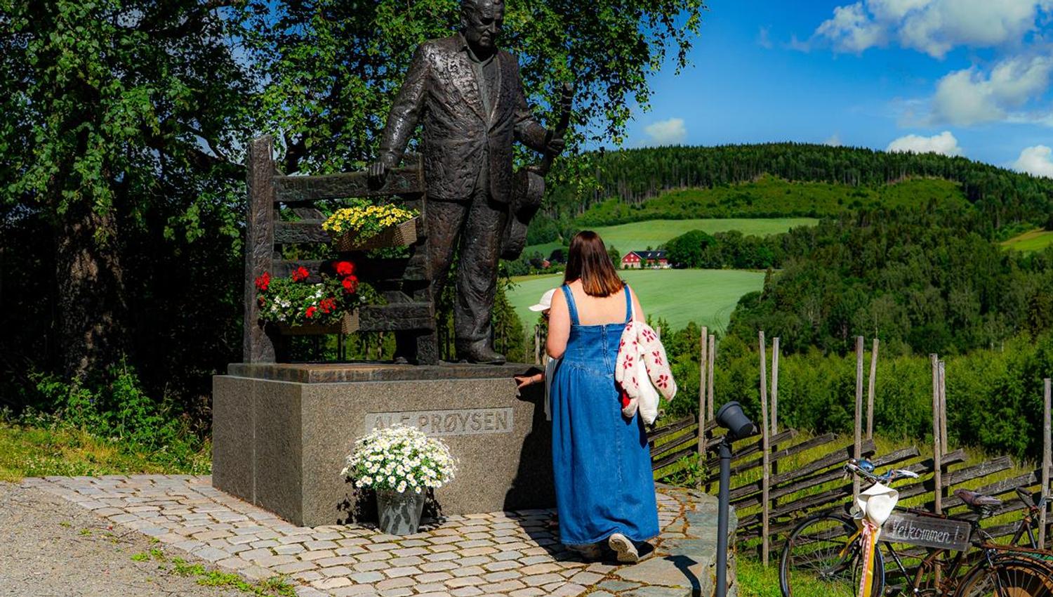 Prøysenhuset i Ringsaker. Mor og sønn foran statue av Alf Prøysen ved inngangen
